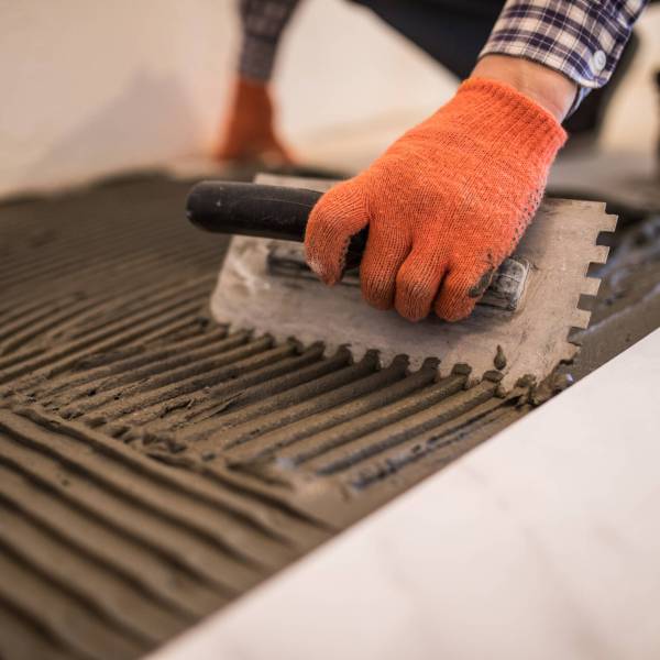 Troweling mortar onto a concrete floor in preparation for laying white floor tile.