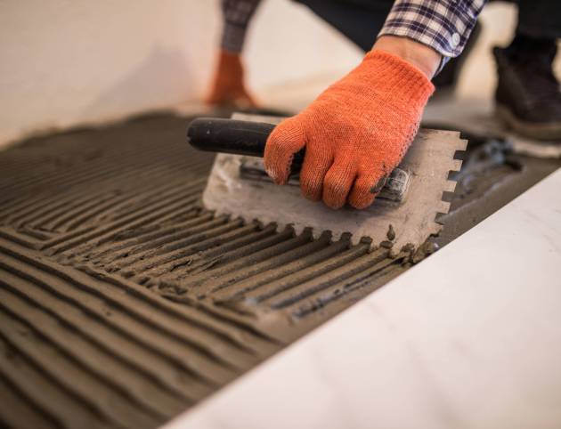 Troweling mortar onto a concrete floor in preparation for laying white floor tile.