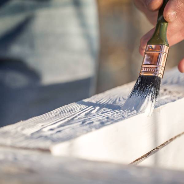 male hand paints with white paint on wood, painting concept, close-up, place for text